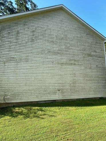 Side view of a house with weathered siding and a grassy lawn under a clear blue sky.