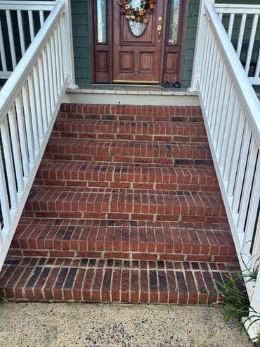 Brick stairs leading to a wooden front door, surrounded by a white railing and porch.