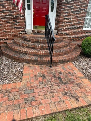 Brick steps leading to a red front door with black railing and landscaped edges.