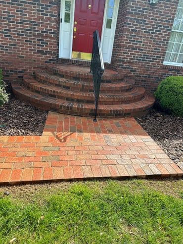 brick steps leading to a red front door with a black railing and landscaped yard