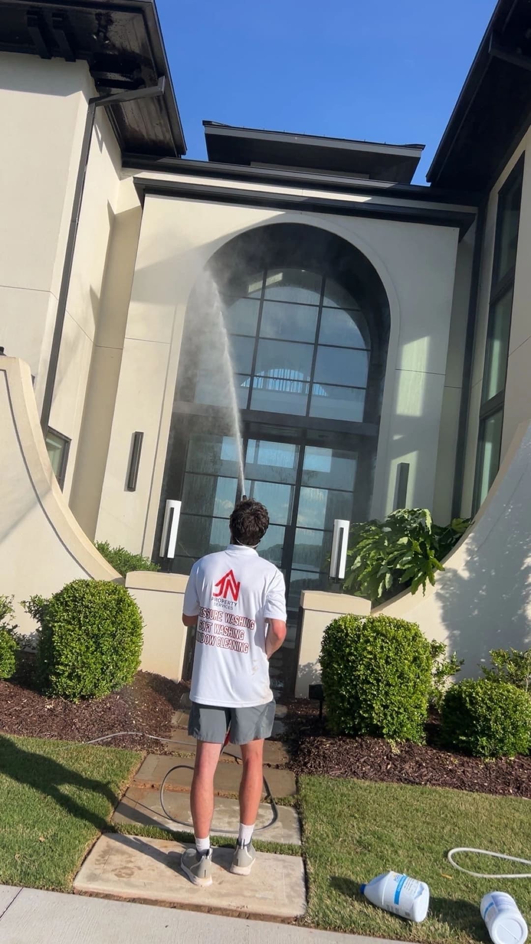 Person cleaning a modern house exterior with a pressure washer on a sunny day.