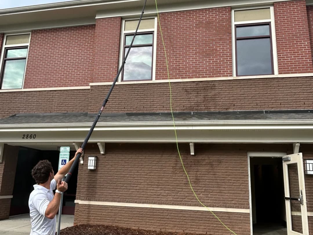Person using a long pole to clean windows on a brick building exterior.