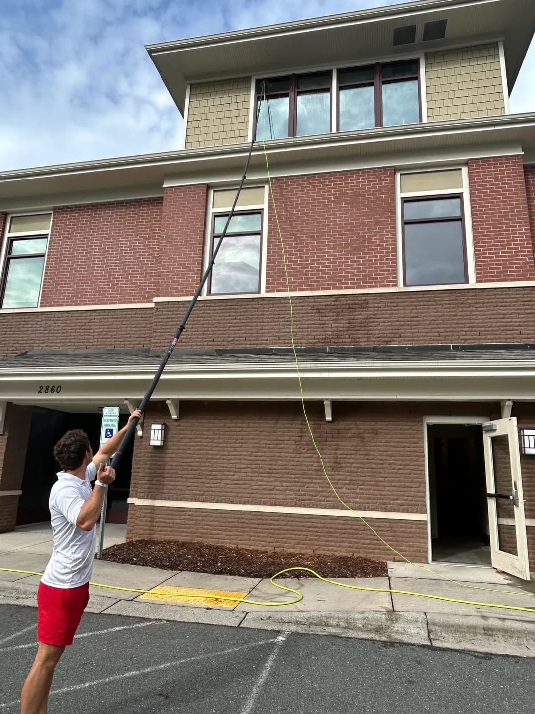 Person using a pole tool to clean windows on a two-story building exterior.