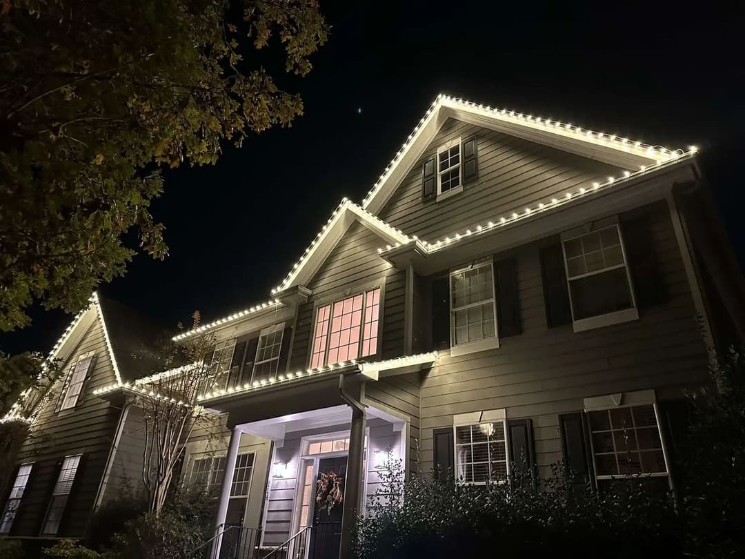 Modern house illuminated with festive lights at night, showcasing elegant architecture and landscaping.