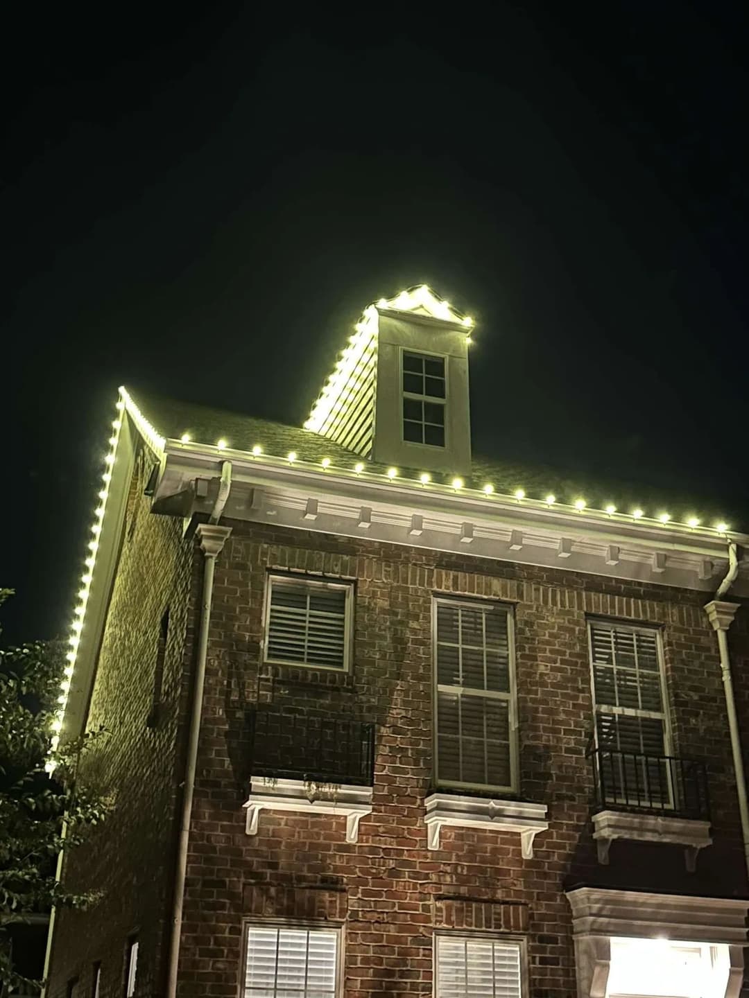 Brick house at night adorned with warm white lights along the roofline.
