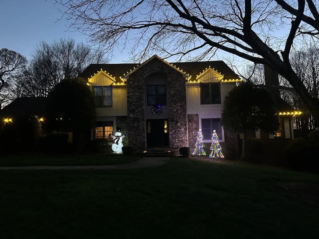 Decorated house at night with Christmas lights, featuring a snowman and two lit trees.